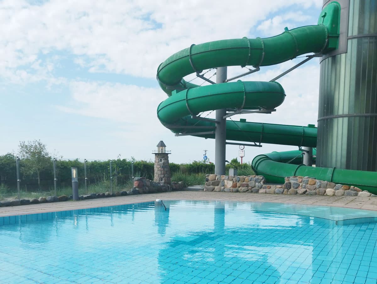 Grüne Wasserrutsche mit mehreren Kurven neben einem leeren Schwimmbecken im Außenbereich