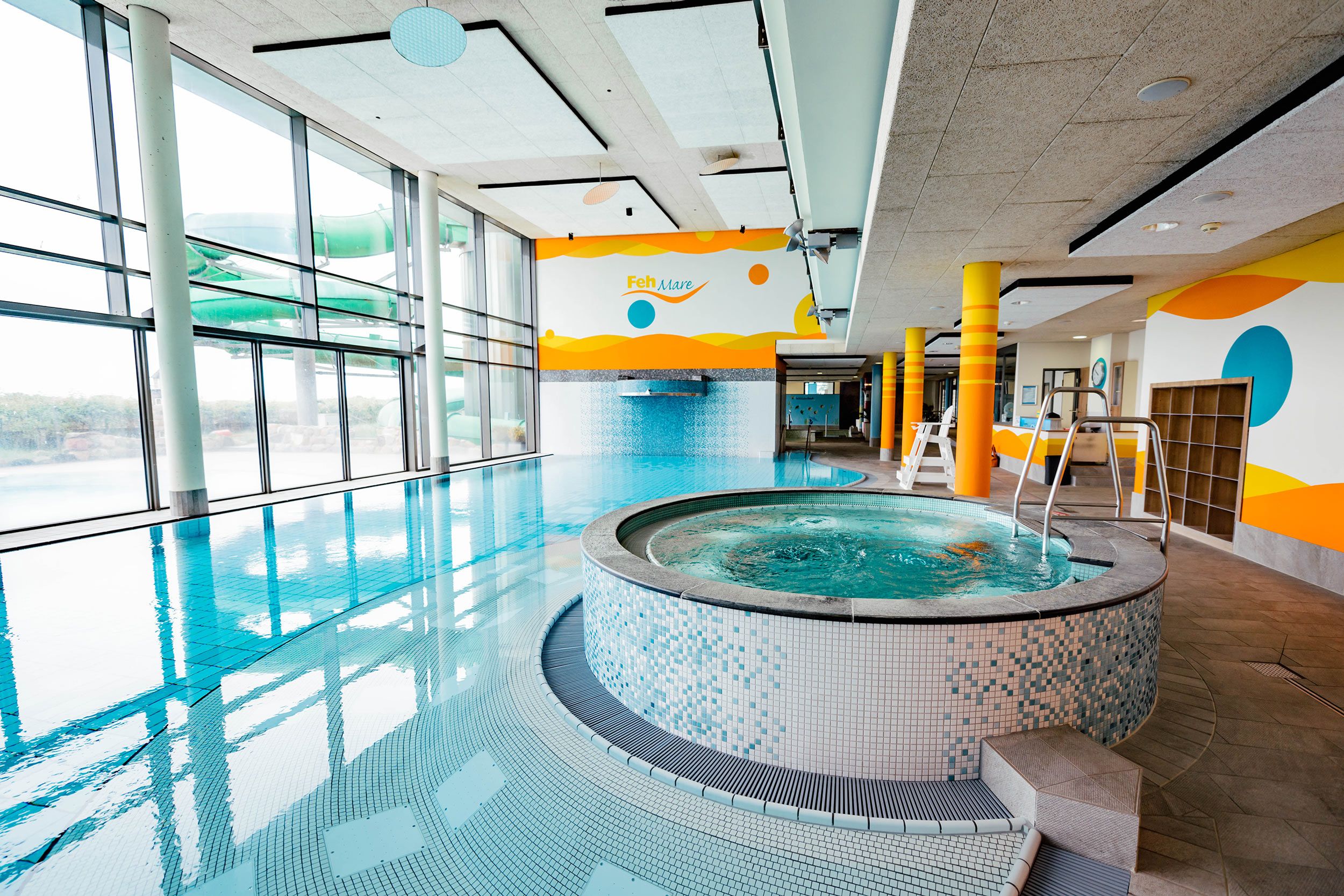 Innenansicht eines Schwimmbads mit großem Whirlpool und Rutsche, große Fenster mit Blick auf Außenbereich