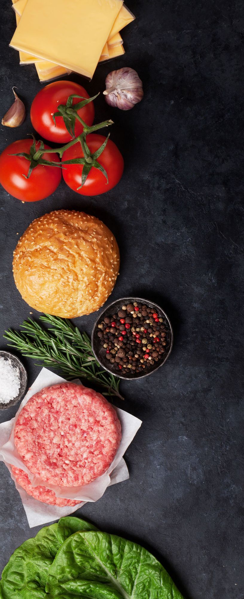 Frische Zutaten für Hamburger: Tomaten am Stiel, Knoblauch, Sesambrötchen, gemischte Pfefferkörner, Rosmarin, rohes Hackfleisch und Salatblatt
