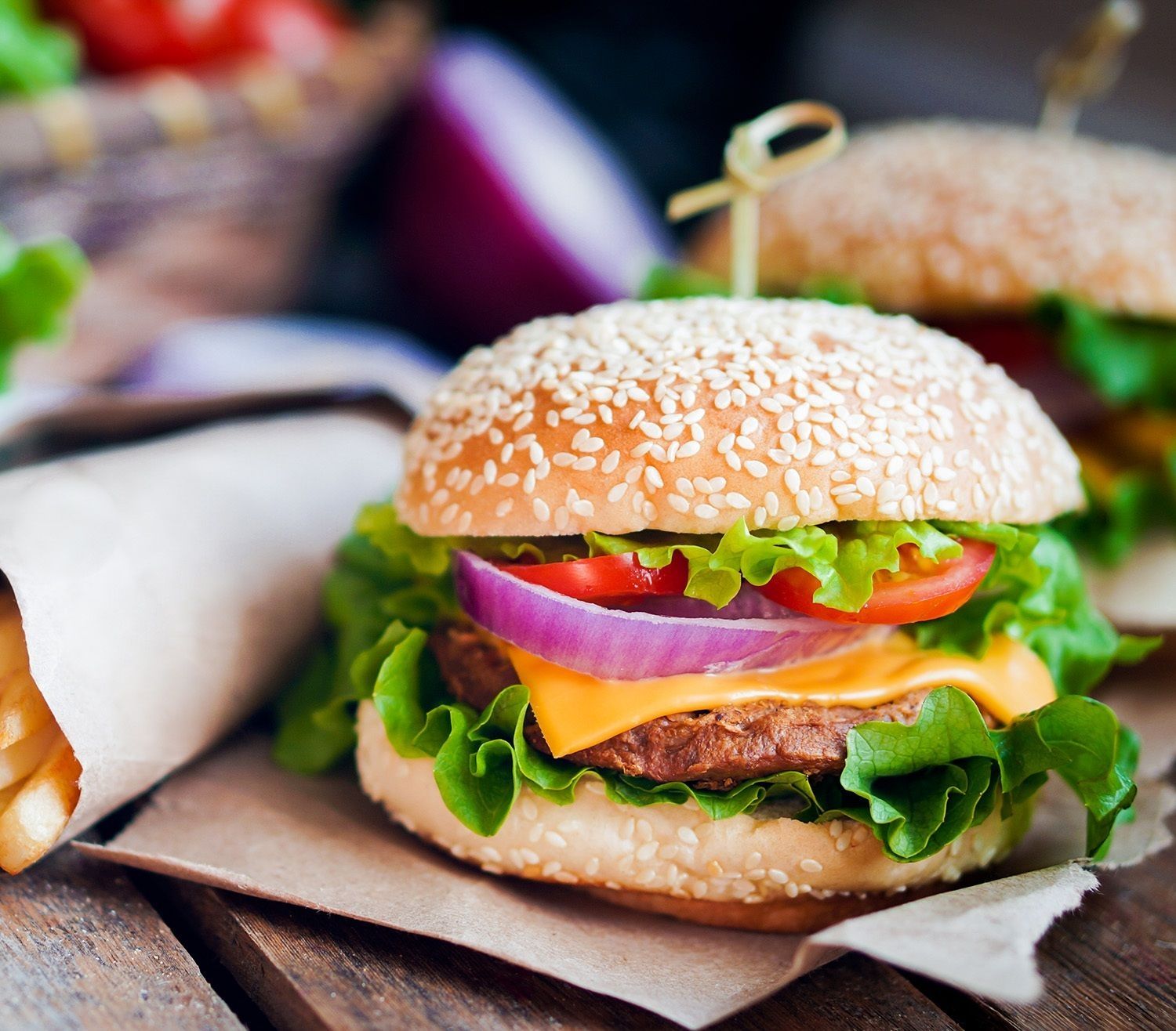 Hamburger mit Sesambrötchen, Salat, Tomate, roter Zwiebel, Cheddarkäse und Rindfleischpatty auf braunem Papier